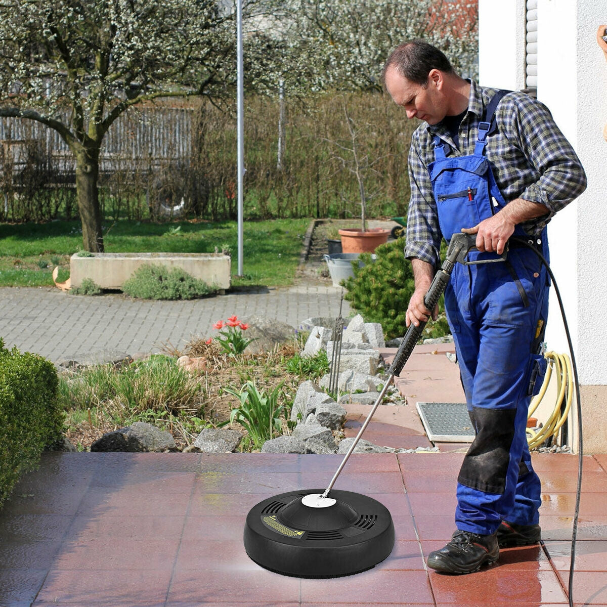A person guides the round surface cleaner over a paved patio with a pressure washer wand.