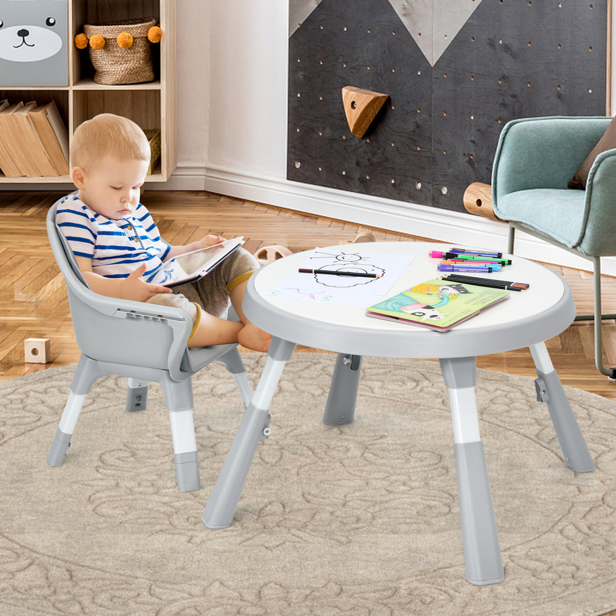 A child sits in a gray highchair beside a low white table in a playroom.