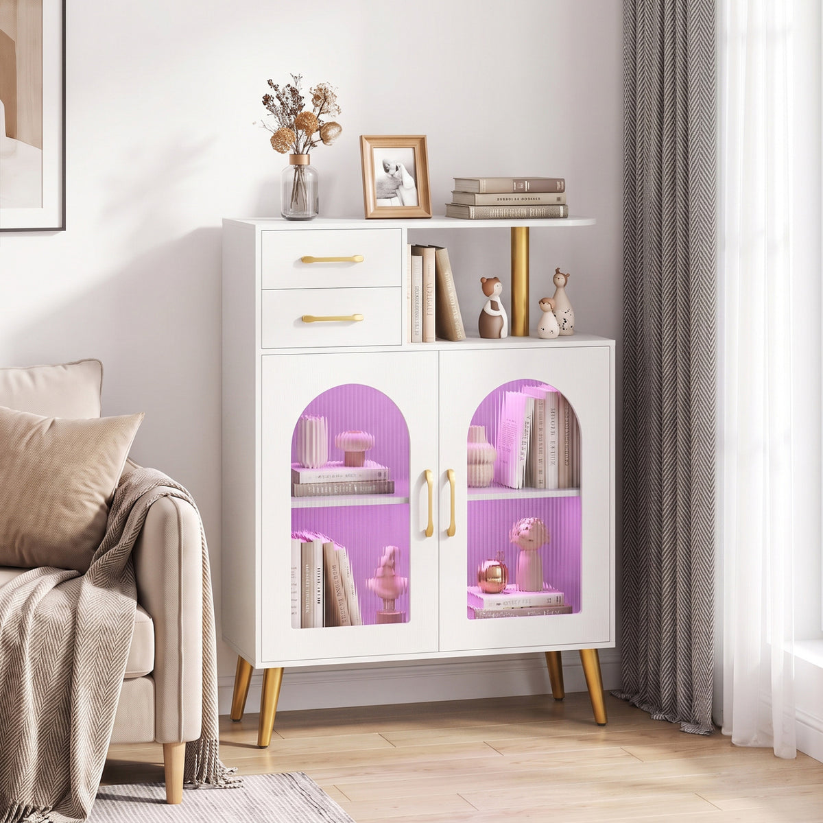 White sideboard with gold legs and translucent doors styled beside a sofa and bright window.