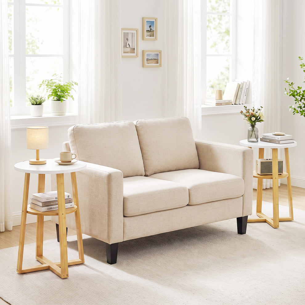 Two white-topped end tables with natural wood frames flank a sofa in a bright living room.