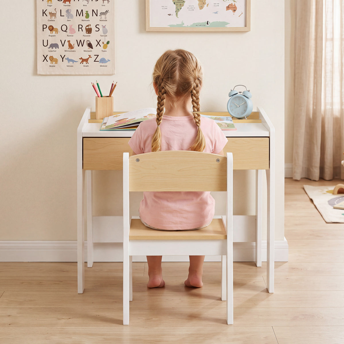 A child sits facing the desk, seen from behind, with books and pencils on the desktop.