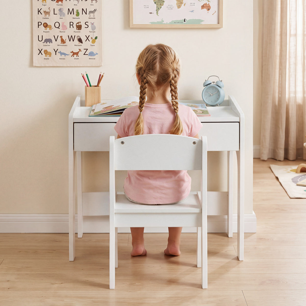 A child sits facing the white desk, with a book and pencil cup on top.