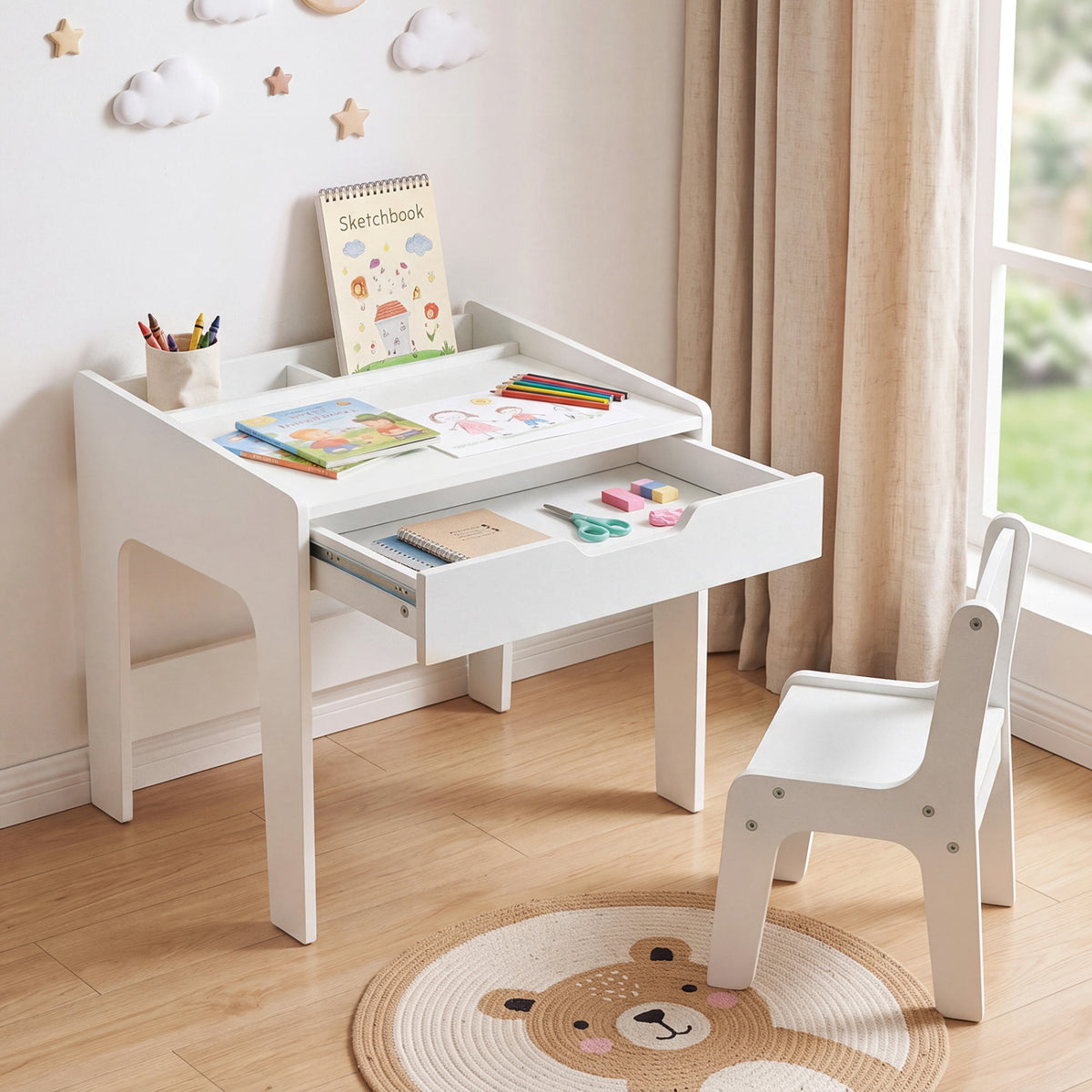 White children's desk with its drawer open and a matching chair in a bright room, arranged with art supplies.