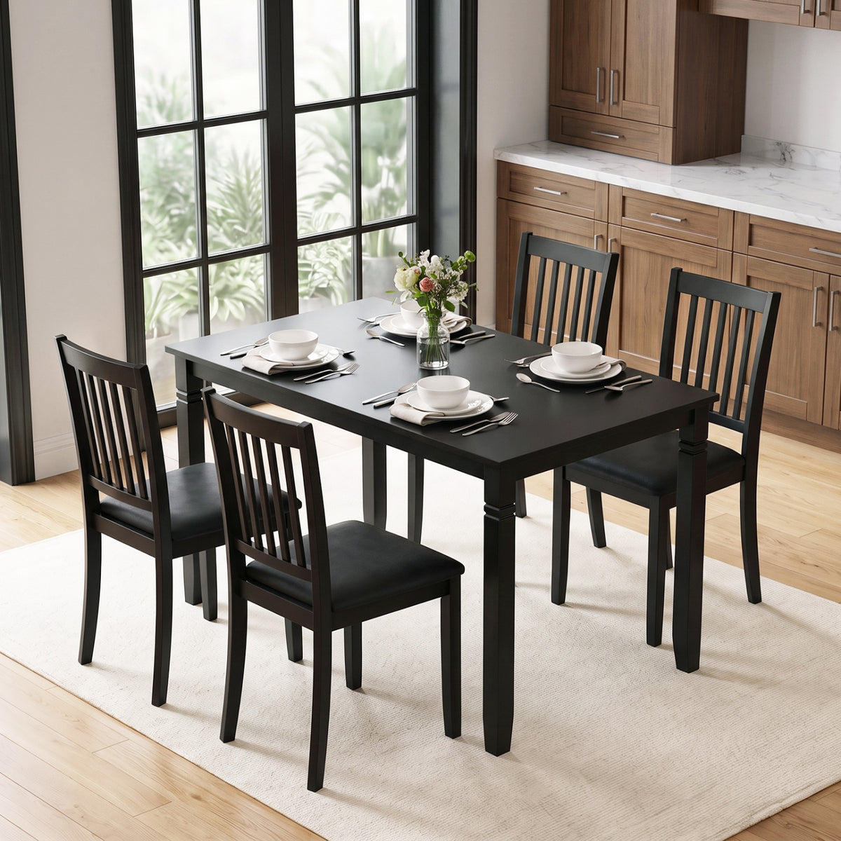 Black dining table set with four slat-back chairs in a bright kitchen, styled with place settings.