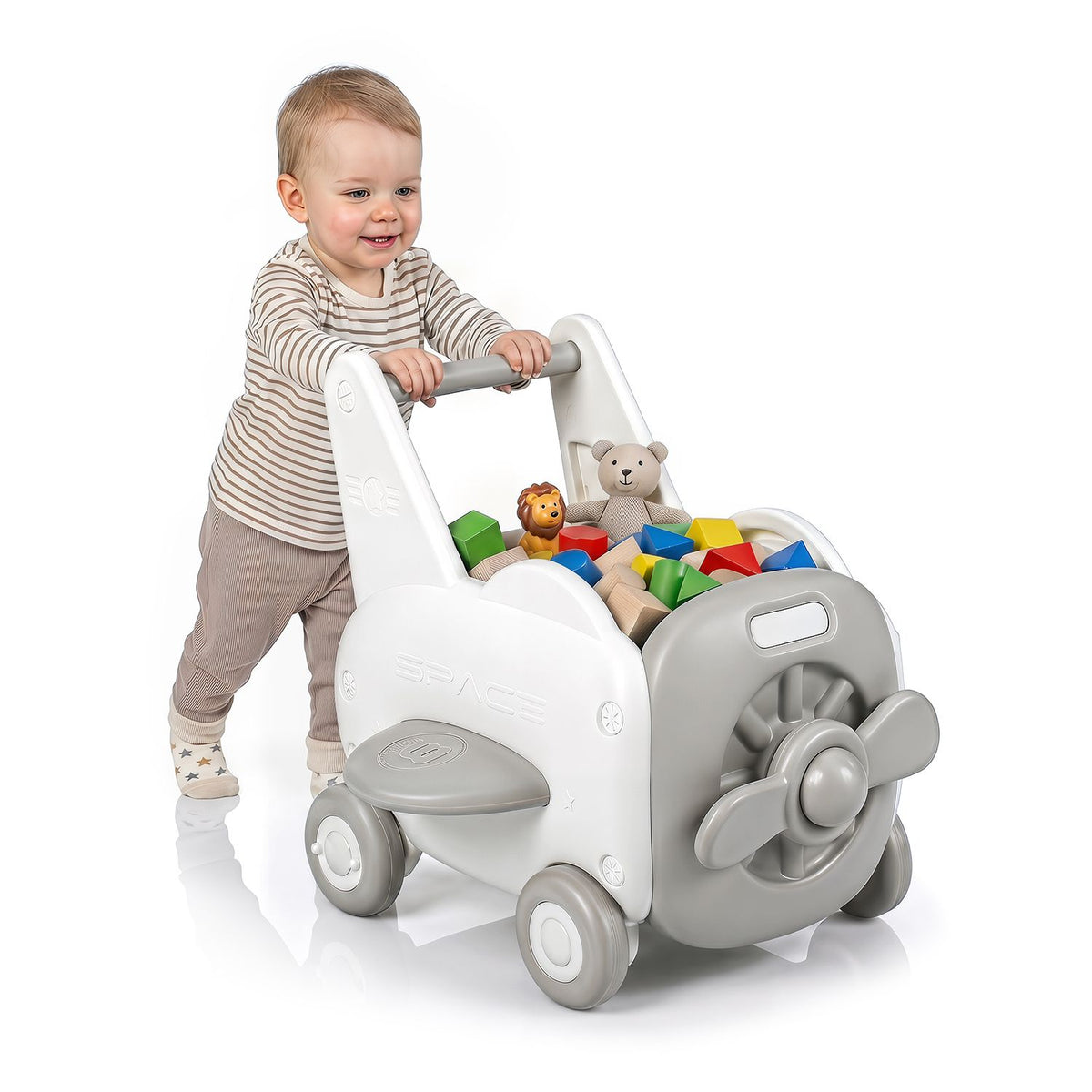 A toddler pushes the walker filled with colorful toys against a white background.