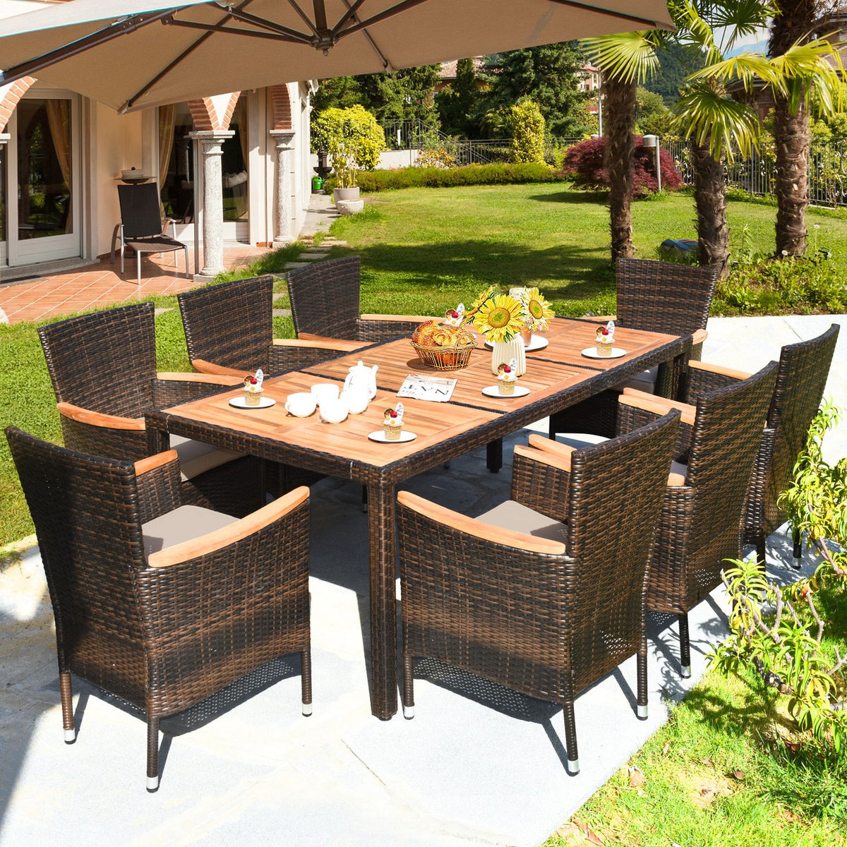 A rectangular wood-top table and woven chairs sit beneath a patio umbrella in a garden.