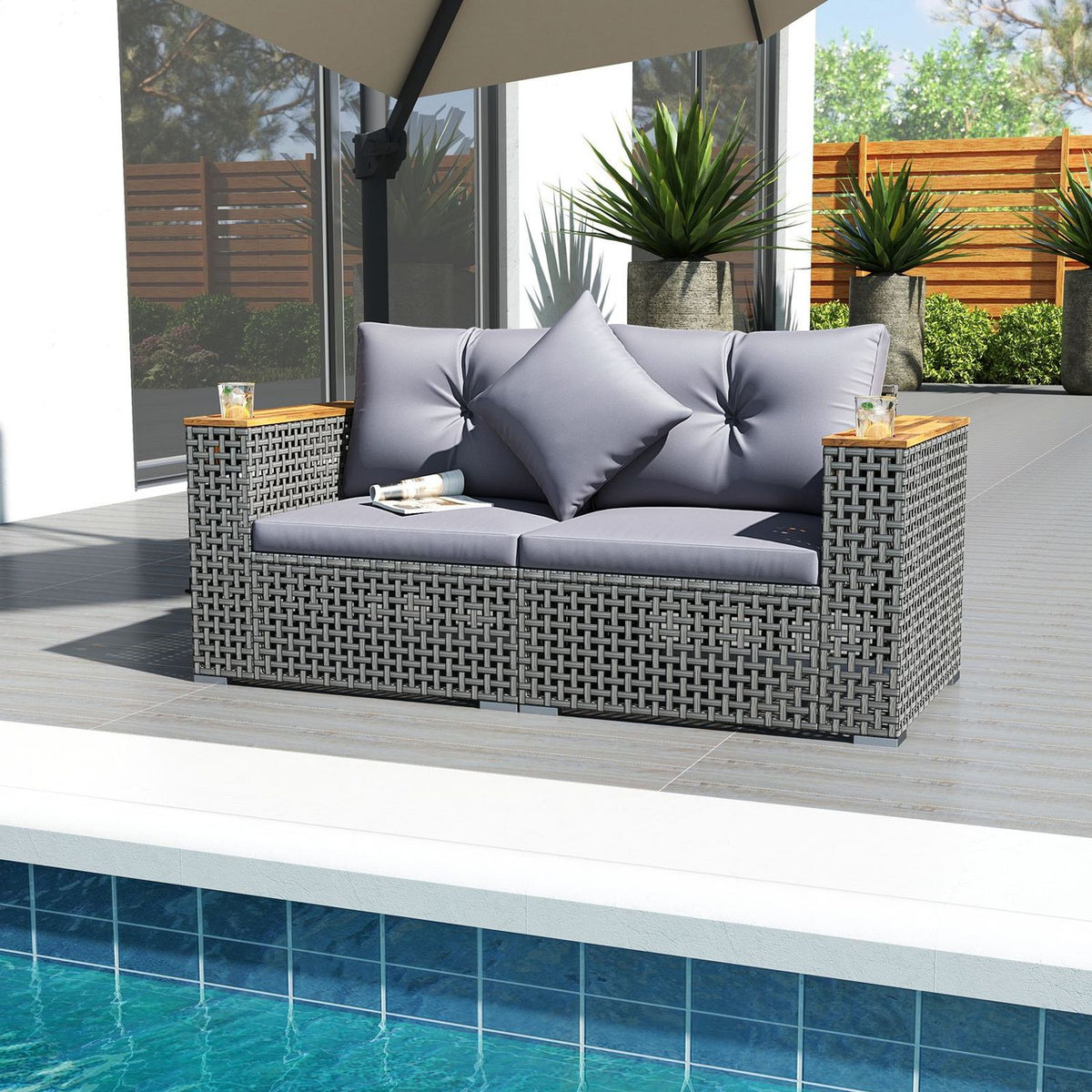 Gray woven loveseat beneath a patio umbrella beside a swimming pool, with small items on its armrests.