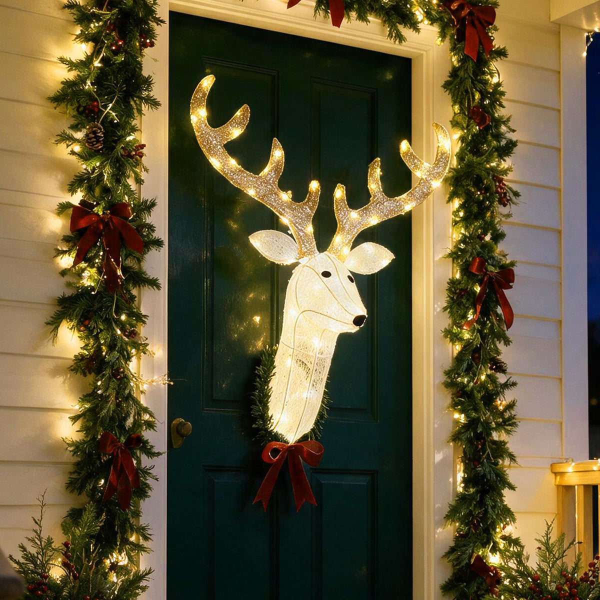 Glowing reindeer head wreath with glittering antlers hangs on a dark green door framed by lit garland.