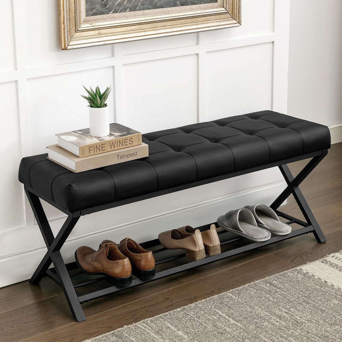Black faux-leather tufted bench top with stacked books and slippers on the shoe shelf below, right-side angle
