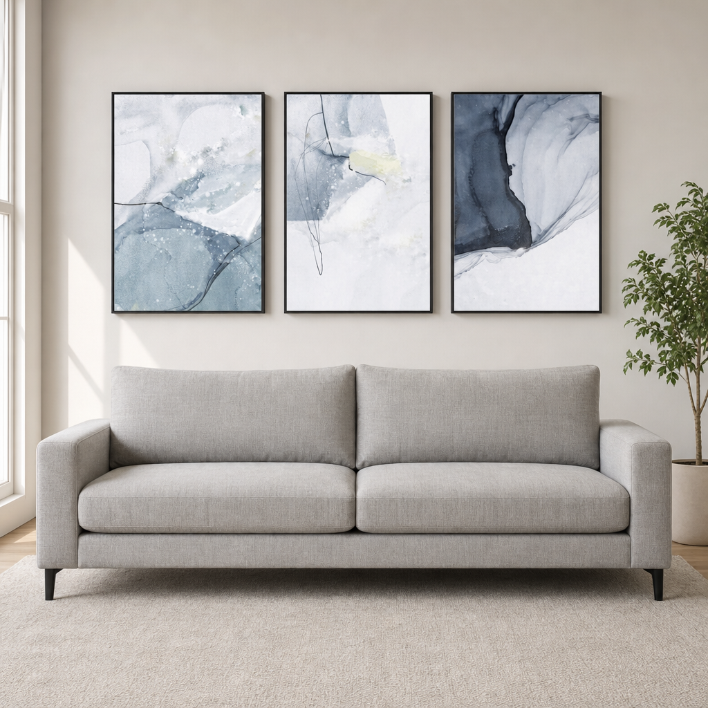 Three framed abstract blue-gray canvases hung above a light gray sofa, straight-on living room view