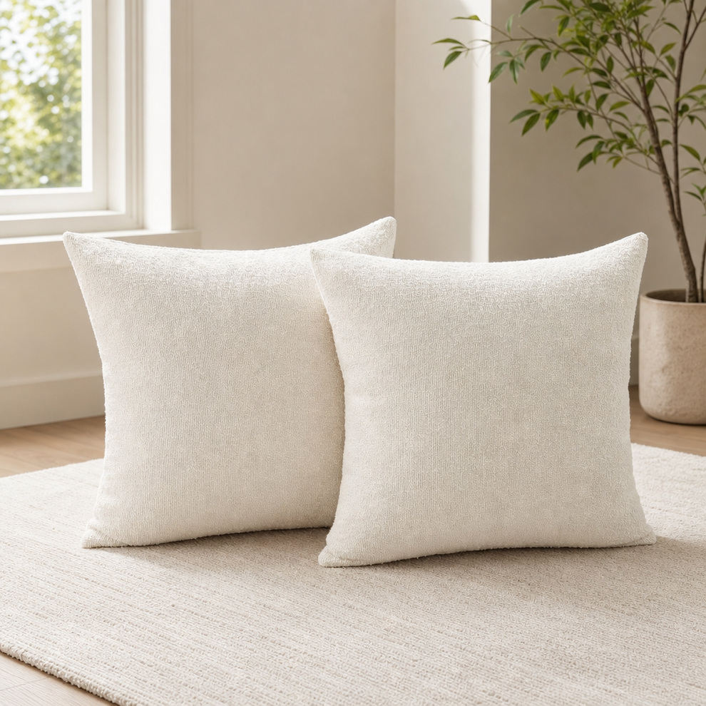 Two ivory boucle pillow covers side-by-side on a textured rug near a window