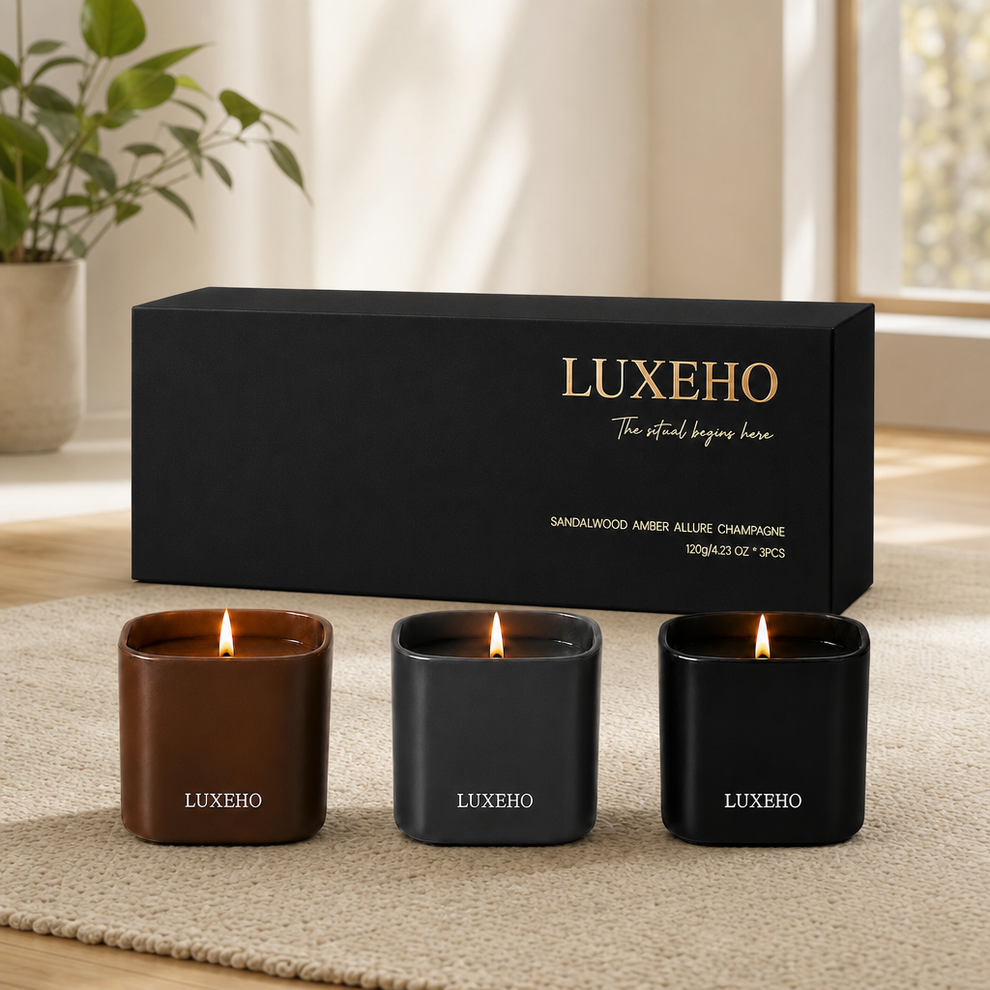 Three lit matte jars in brown, gray and black arranged before a black gift box on a textured rug in a living room.
