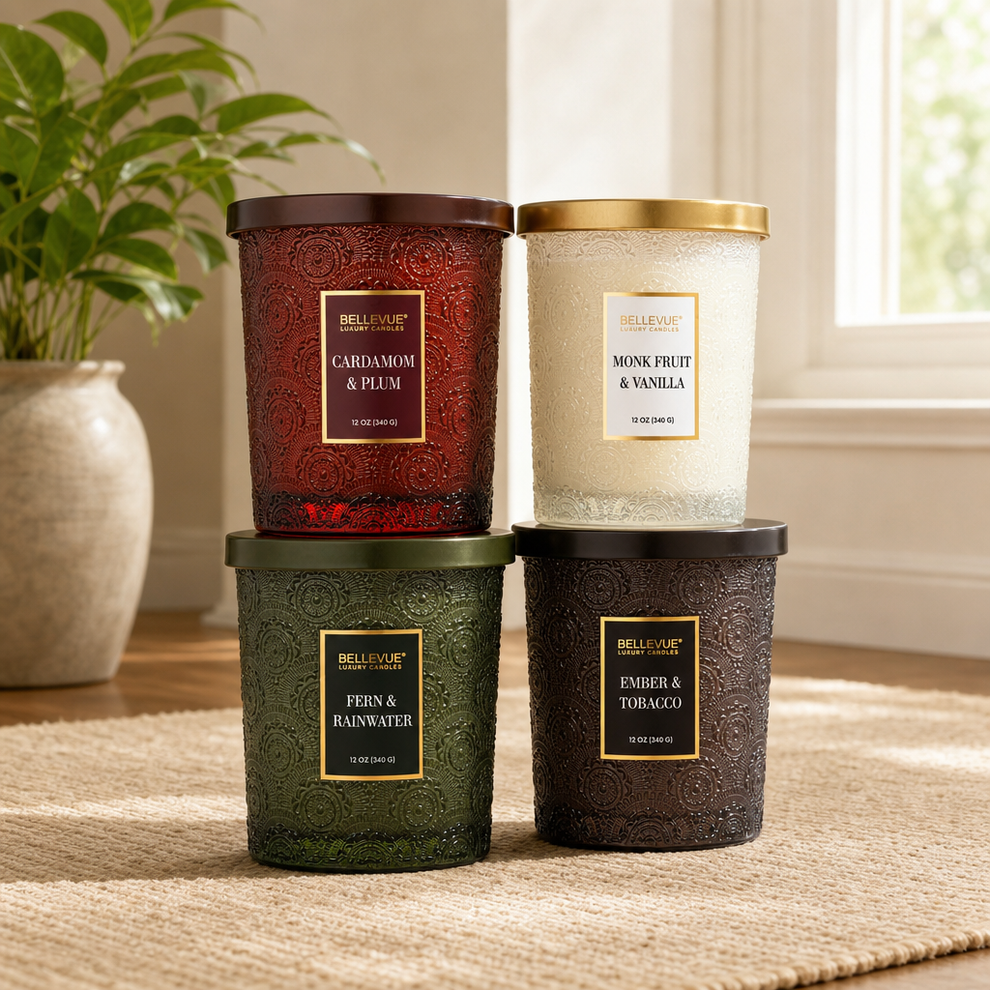 Four embossed glass jar candles in red, green, white and dark brown arranged stacked on a rug, angled front view