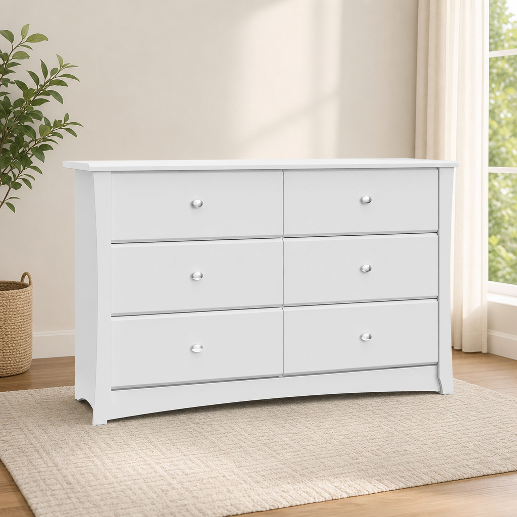 White 6-drawer dresser angled front view on a rug with a plant and window in the background
