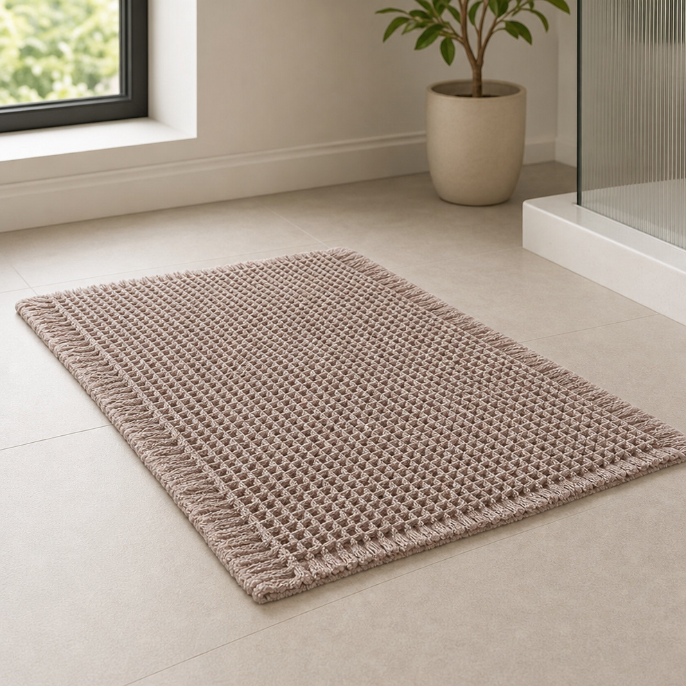 Taupe waffle bath mat shown at an angle on a tiled bathroom floor