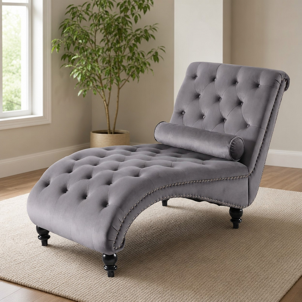 Grey tufted chaise lounge with bolster pillow, angled view in a bright living room
