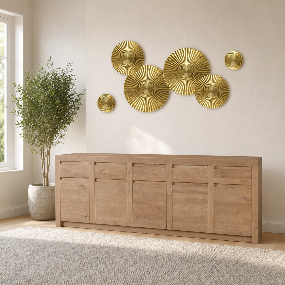 Glossy gold circular sunburst metal wall sculptures grouped above a wooden console with a potted plant