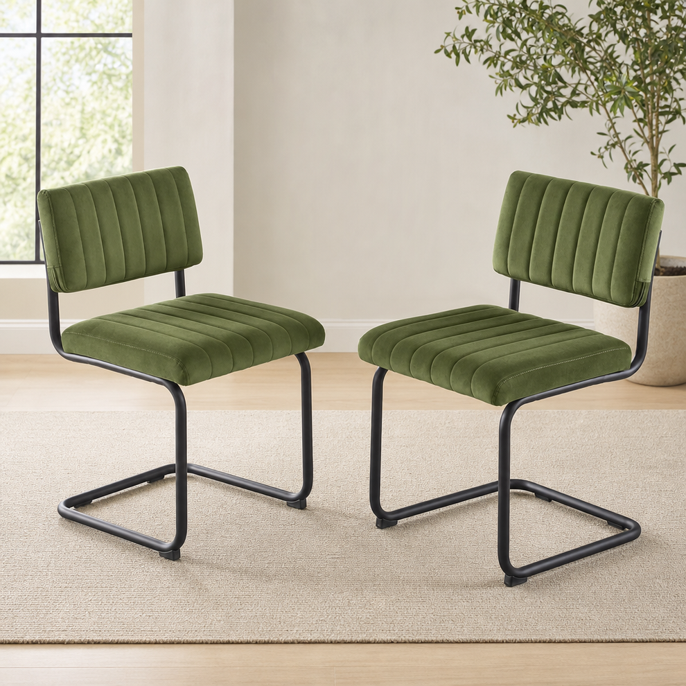 Pair of green velvet armless cantilever dining chairs, angled front view showing tufted seats and black steel frames