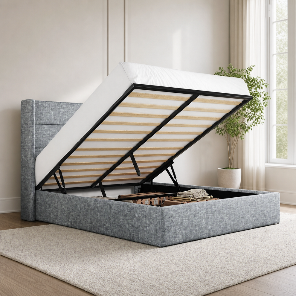 Grey upholstered wingback bed with mattress lifted to reveal open under-bed storage, angled front-left view