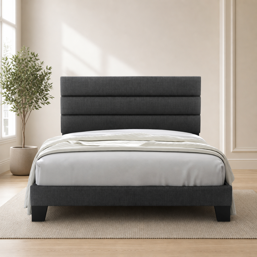 Dark grey fabric platform bed with horizontal padded headboard front view in a bright bedroom with a potted plant