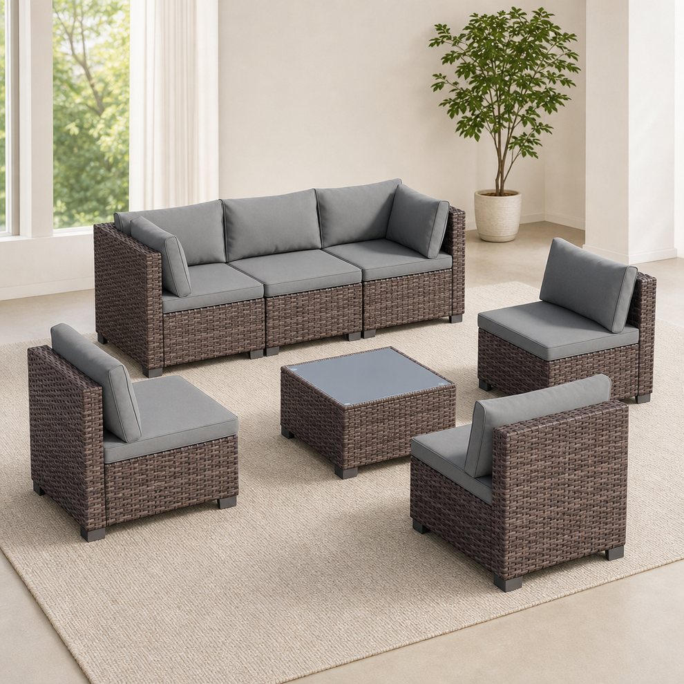 Brown PE rattan 7-piece outdoor sectional with grey cushions and square glass-top table, angled front view in a bright room
