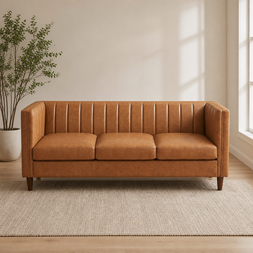 Cognac tan three-seat faux leather sofa front view on a neutral rug with a potted plant to the left.