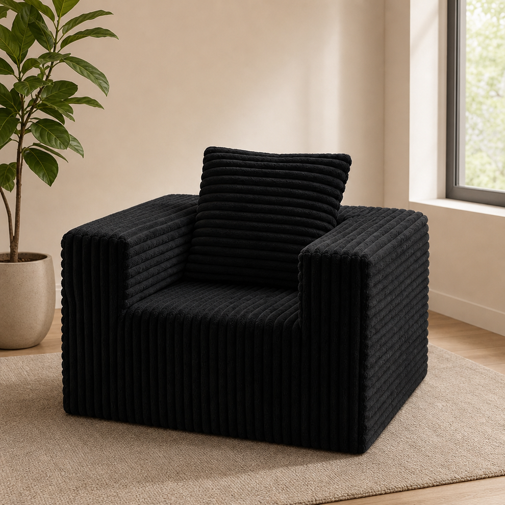 Black corduroy floor chair angled front view on a neutral rug beside a potted plant and window.
