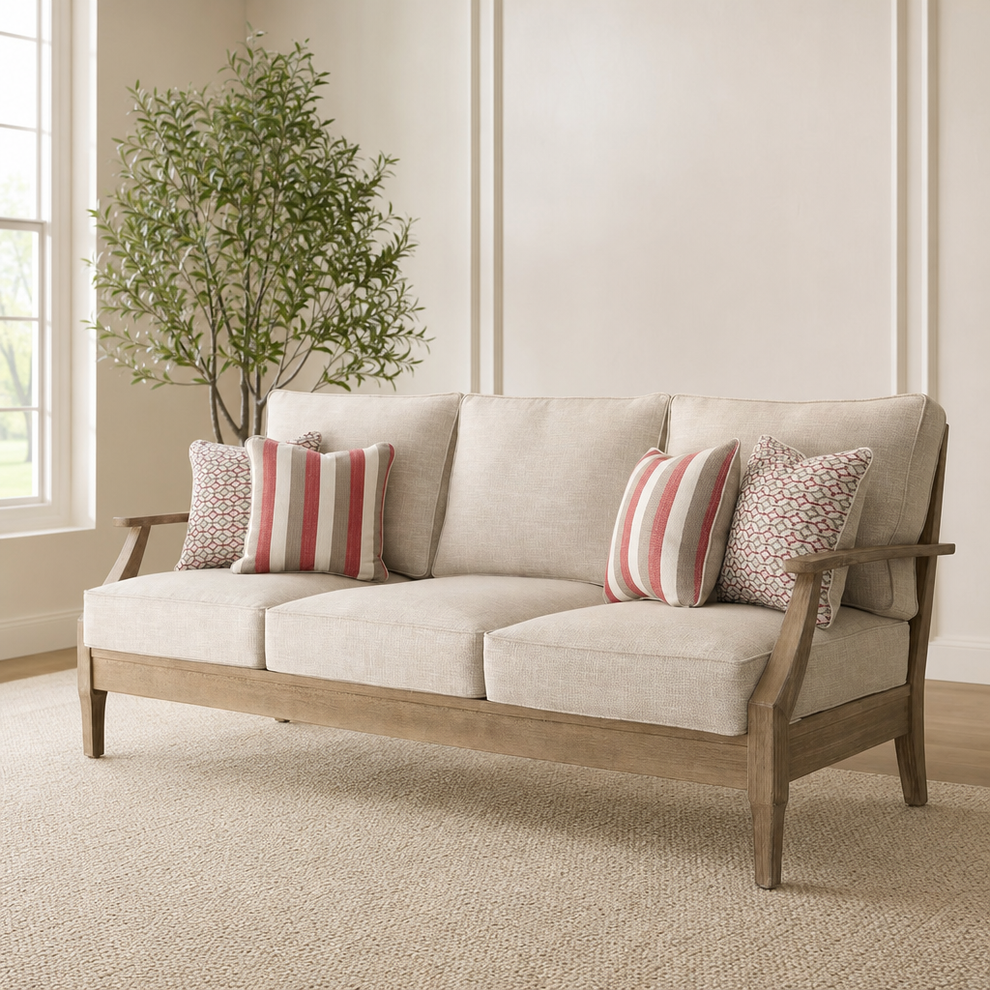 Beige three-seat outdoor sofa front angled view indoors showing tapered arms and four patterned throw pillows