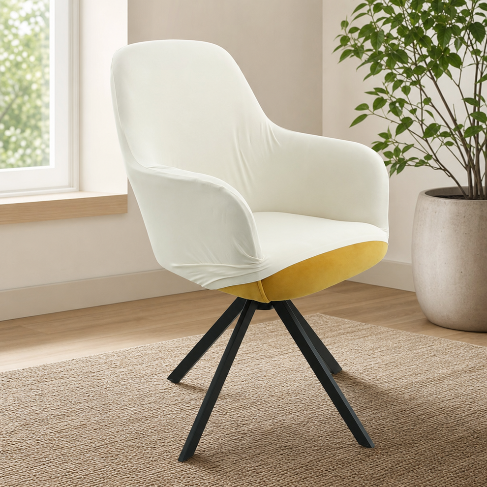 White stretch slipcover on a mid-back armchair angled front-left beside a window and potted plant