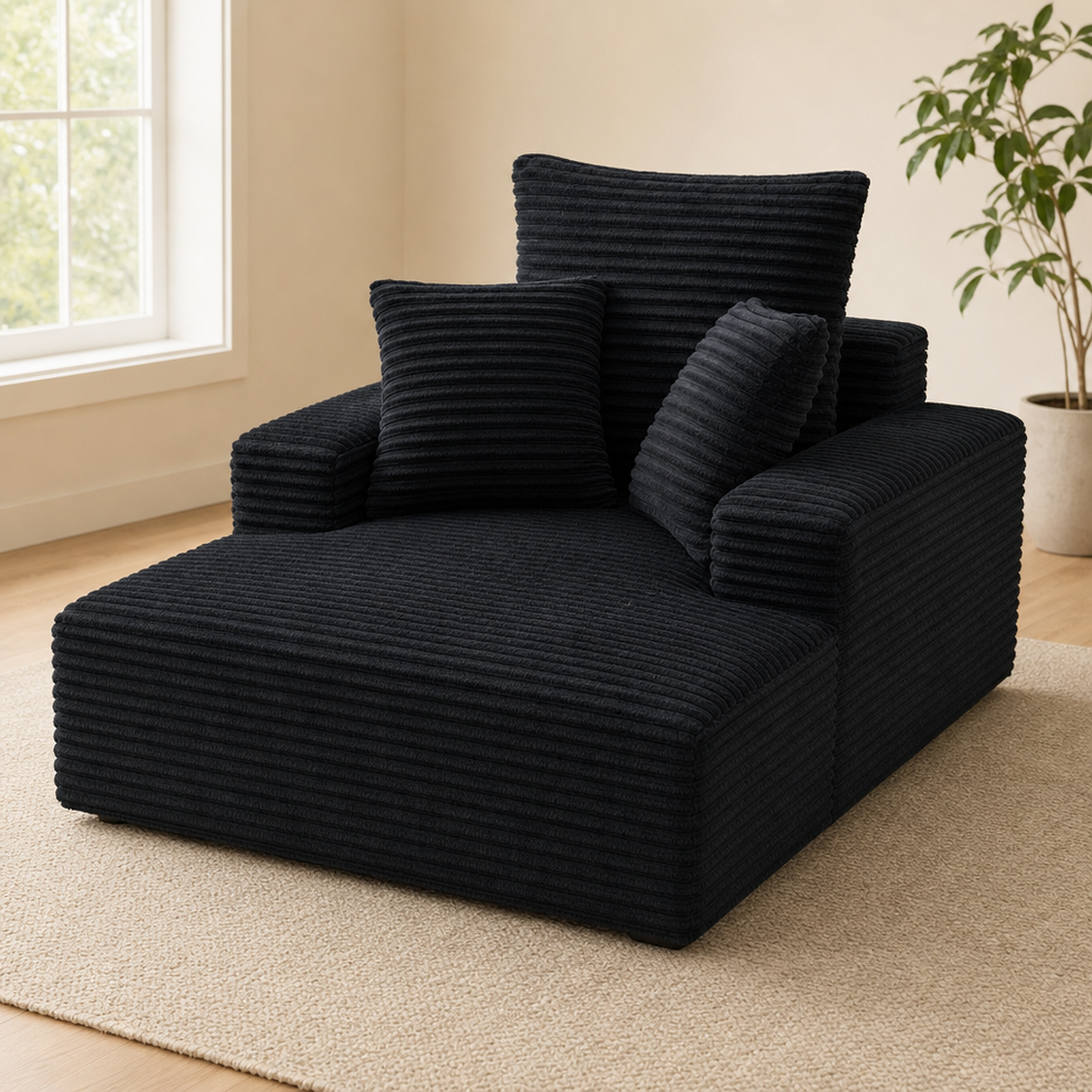 Black corduroy boneless chaise lounge angled front view with three matching throw pillows on a light rug