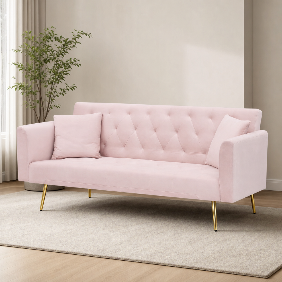 Light pink velvet futon with tufted back and gold tapered legs angled front view in a neutral living room