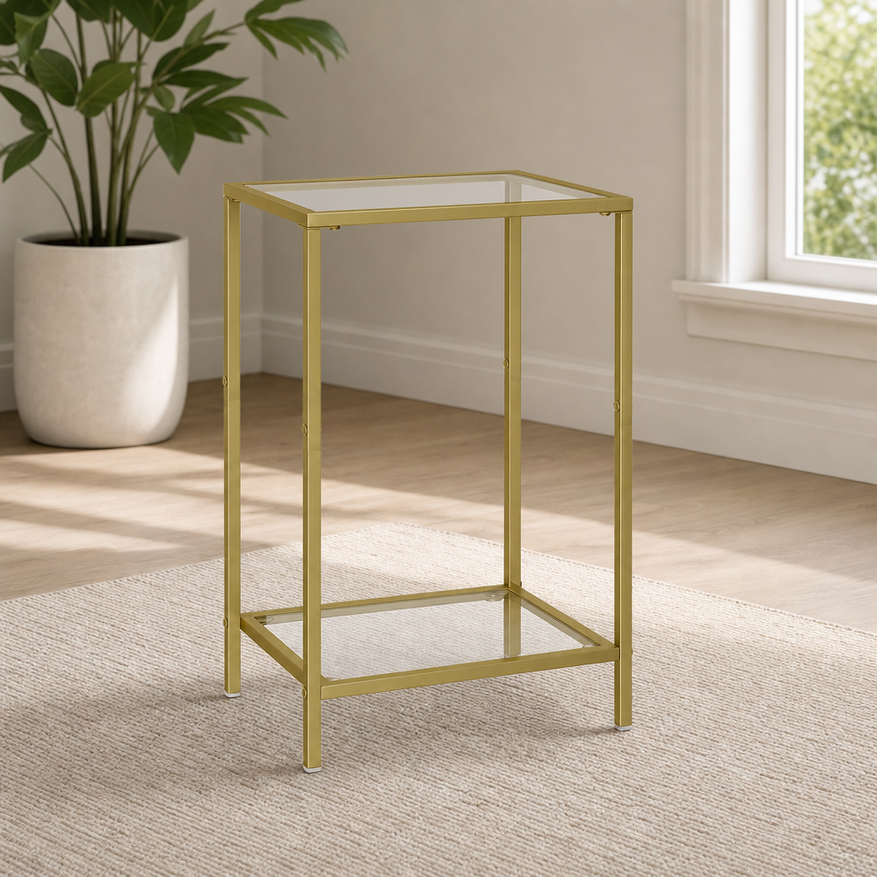 Gold metal 2-tier side table with tempered glass top and lower shelf, angled front view on a rug beside a plant.