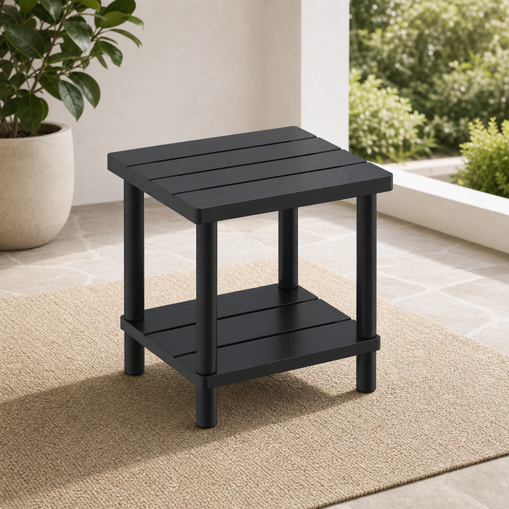 Black bamboo two-tier side table angled front view on a patio rug beside a planter