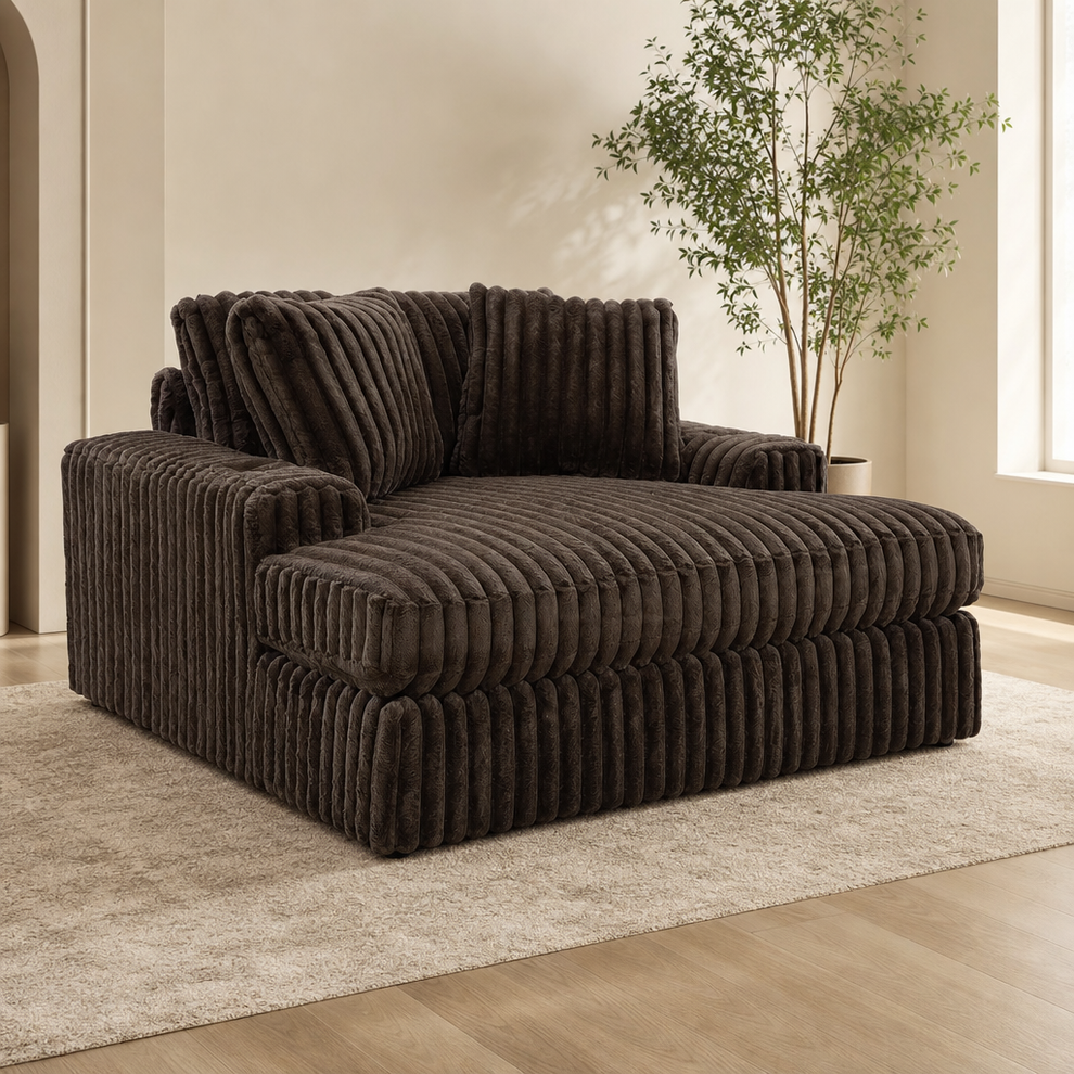 Brown jumbo corduroy oversized chaise lounge angled front view on a light rug with a potted plant in the background