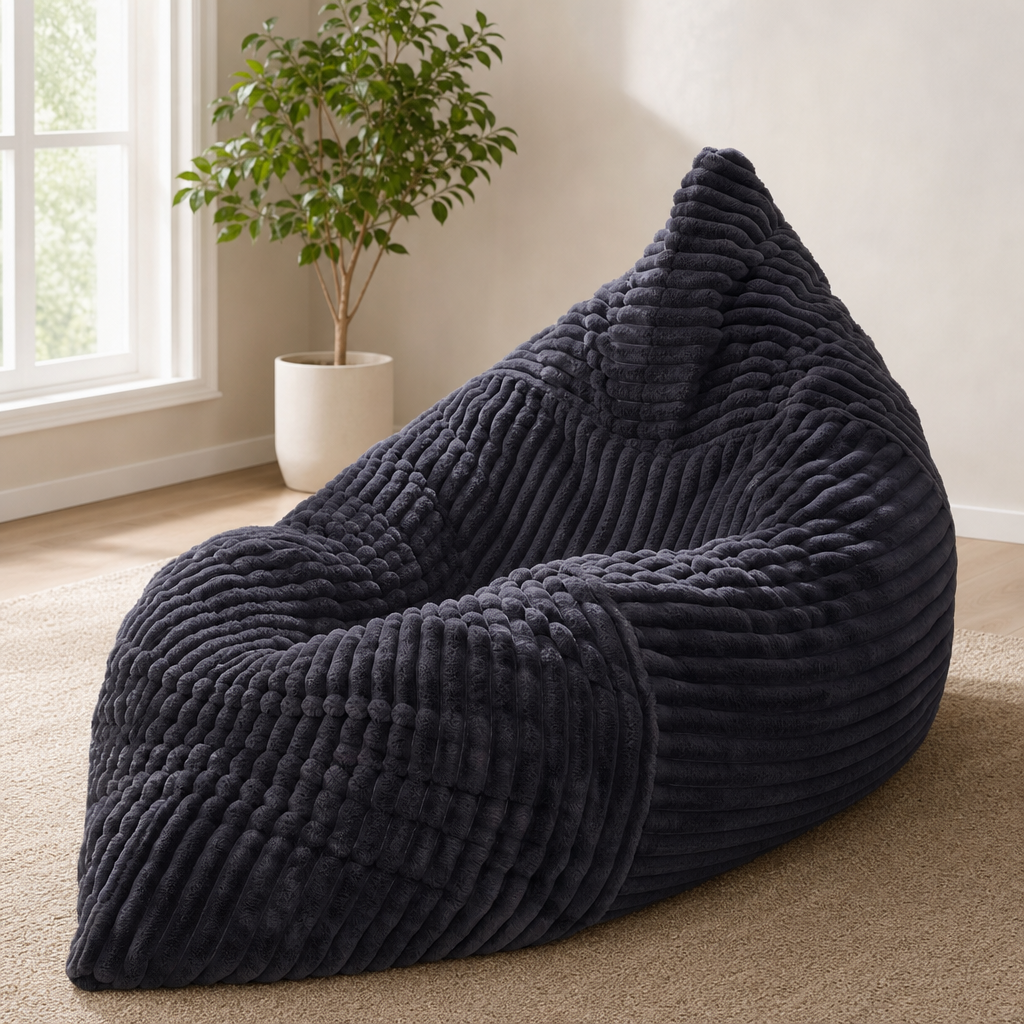 Dark grey corded fabric bean bag chair angled front view on a beige rug beside a potted plant in a living room