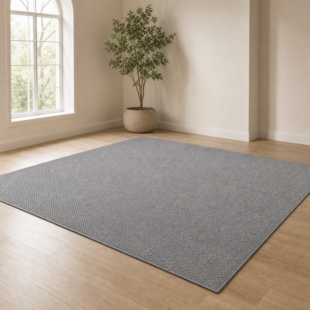 Grey jute-style area rug angled front view on light hardwood floor with arched window and potted plant