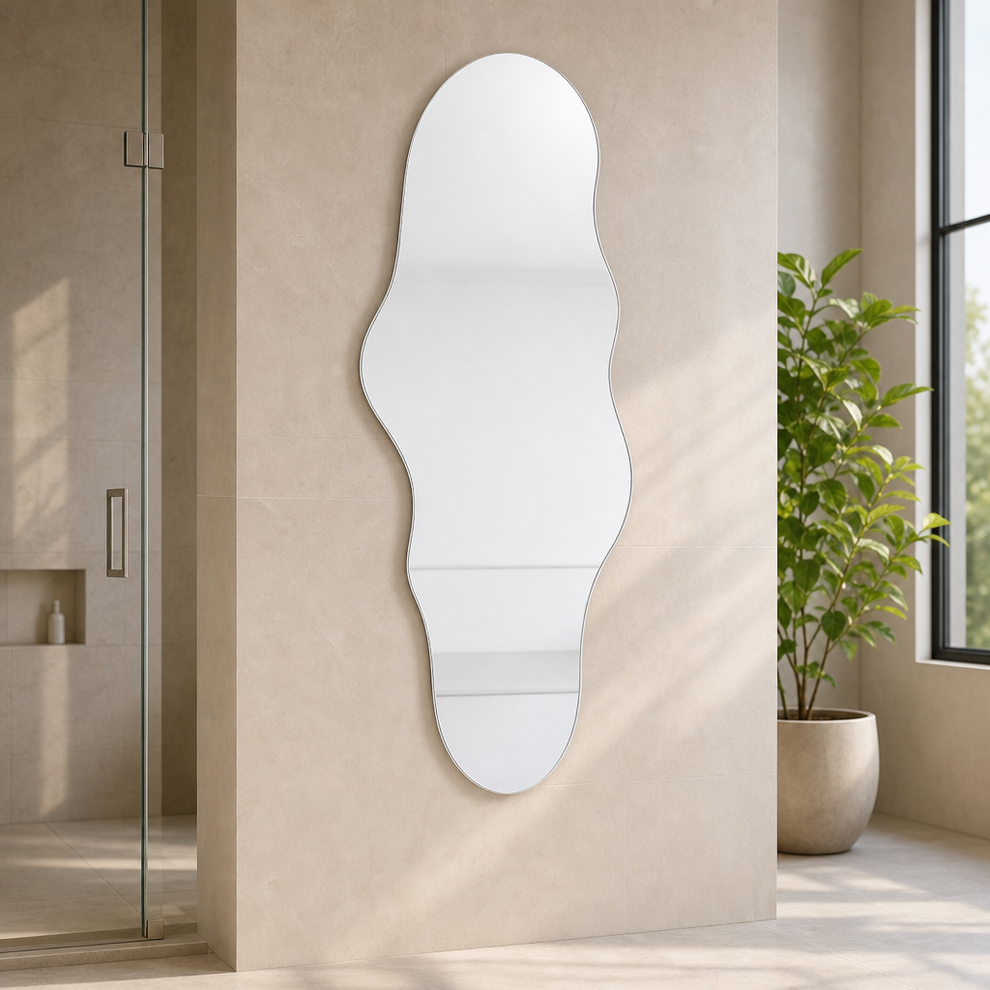 Frameless cloud-shaped mirror mounted on a beige tiled wall beside a glass shower and a potted floor plant
