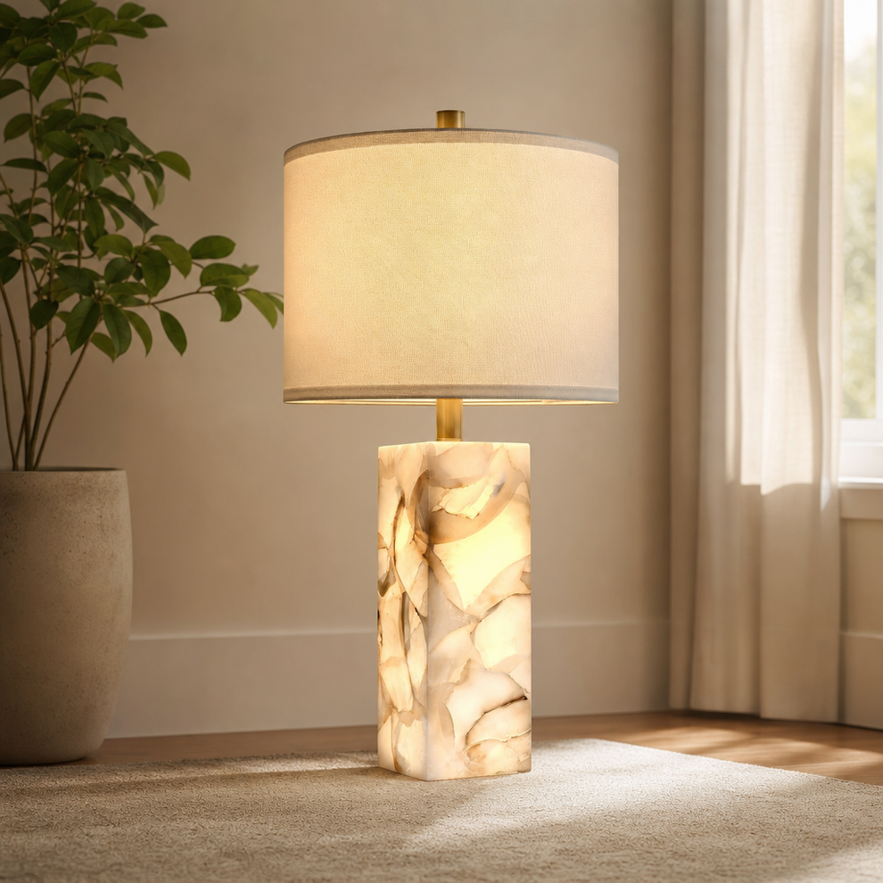 White alabaster column table lamp with white linen drum shade, front view in a bright sitting room