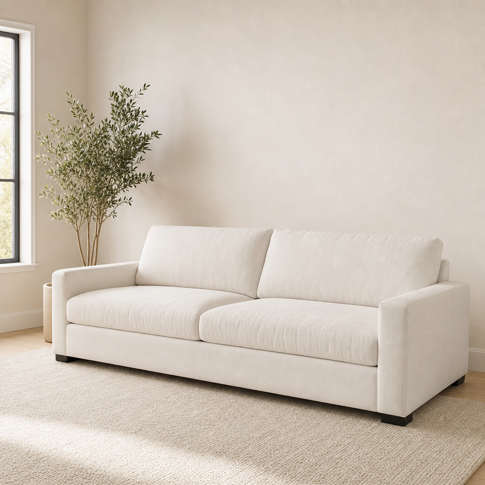 Neutral living room with beige sofa and tall potted plant against an empty wall.