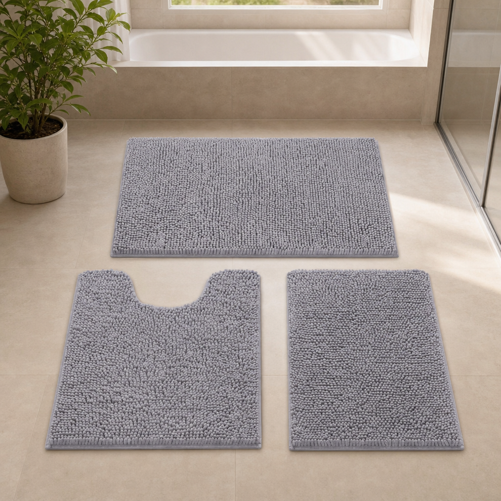 Grey chenille 3-piece bathroom rug set arranged on tiled floor near a bathtub and potted plant, angled top view